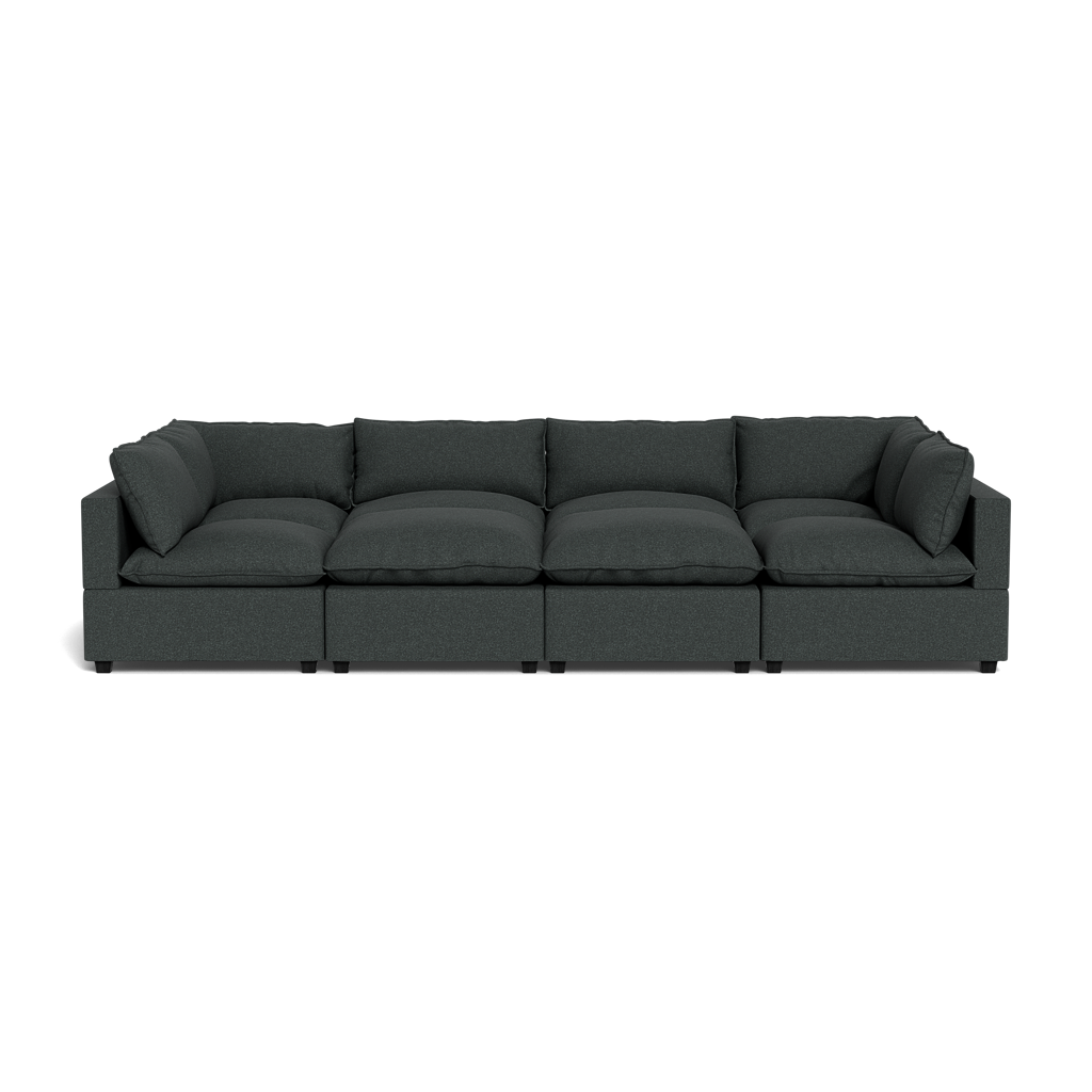 The Kova Pillow Cushion Grand Pit is a modern, dark gray sectional sofa with four seats, plush cushions, and armrests on both ends, shown from the front against a plain black background.