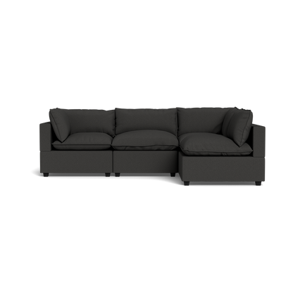 The Kova Pillow Cushion L-Shape is a modern dark gray sectional with three seat cushions, three back cushions, and wide armrests, displayed against a plain black background.