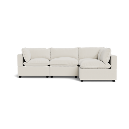 The Kova Pillow Cushion L-Shape is a modern, light beige sectional sofa featuring three seat cushions and five matching backrest pillows, displayed against a plain white background.