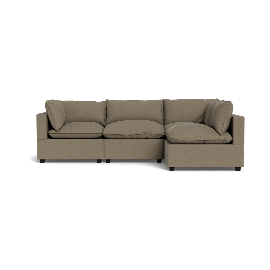 The Kova Pillow Cushion L-Shape is a modern, three-seater sectional sofa in light brown fabric with wide armrests and plush cushions, shown from the front against a plain black background.