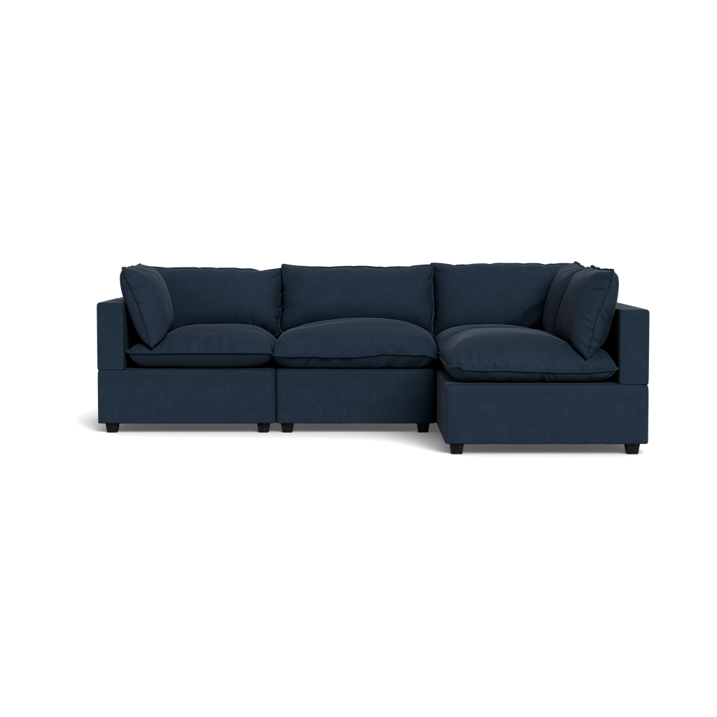 The Kova Pillow Cushion L-Shape is a modern dark blue sectional with three seat cushions, three back cushions, and two side cushions, shown against a plain black background.
