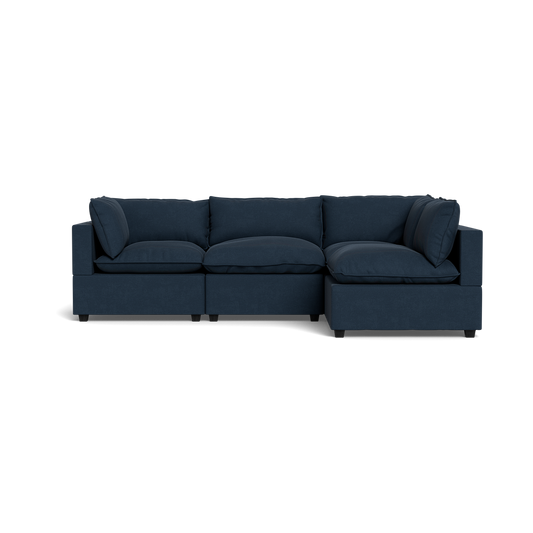 The Kova Pillow Cushion L-Shape is a modern dark blue sectional with three seat cushions, three back cushions, and two side cushions, shown against a plain black background.