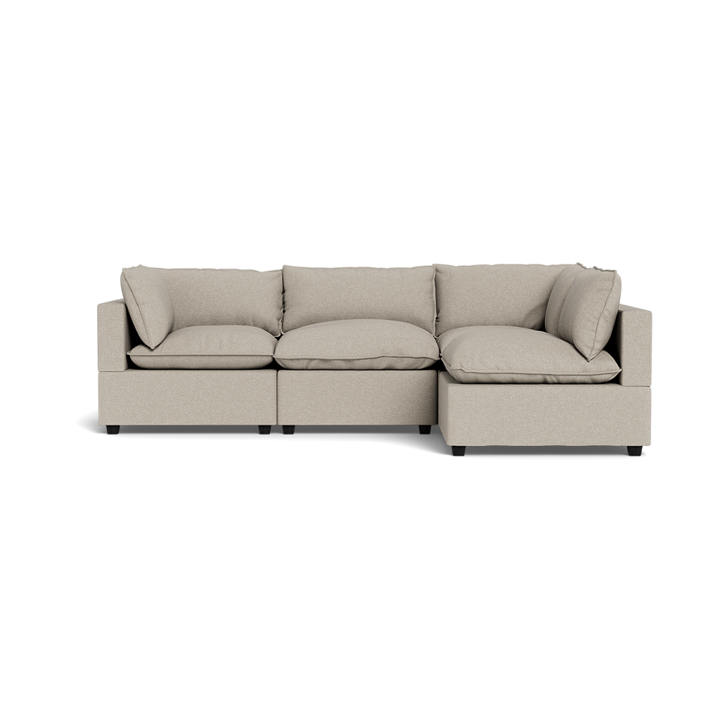 The Kova Pillow Cushion L-Shape is a modern, light beige sectional sofa with three plush seats, shown from the front against a black background.
