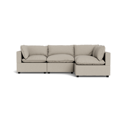 The Kova Pillow Cushion L-Shape is a modern, light beige sectional sofa with three plush seats, shown from the front against a black background.