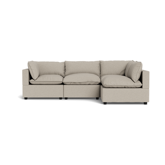 The Kova Pillow Cushion L-Shape is a modern, light beige sectional sofa with three plush seats, shown from the front against a black background.