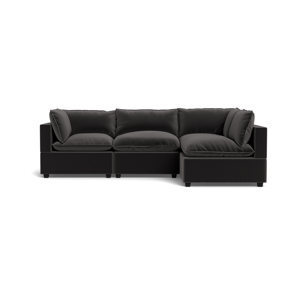 The Kova Pillow Cushion L-Shape is a modern black sectional with three main seats and a right-side chaise lounge, featuring plush back and seat cushions, shown against a plain black background.