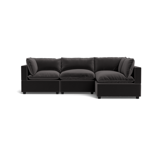The Kova Pillow Cushion L-Shape is a modern black sectional with three main seats and a right-side chaise lounge, featuring plush back and seat cushions, shown against a plain black background.