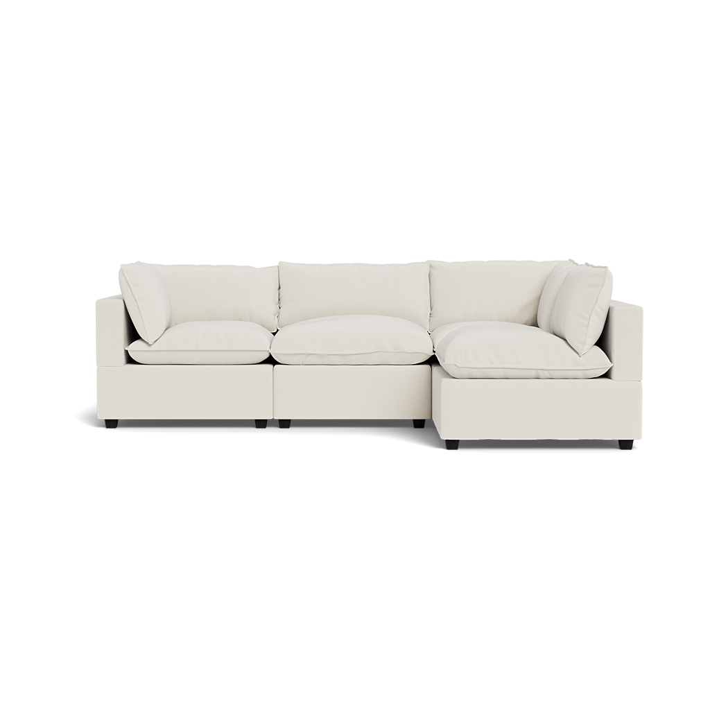 The Kova Pillow Cushion L-Shape is a modern, light beige sectional sofa with plush seat and back cushions, clean lines, and two armrests, displayed on a transparent background.