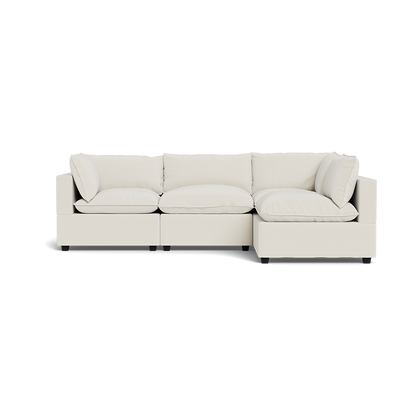 The Kova Pillow Cushion L-Shape is a modern, light beige sectional sofa with plush seat and back cushions, clean lines, and two armrests, displayed on a transparent background.