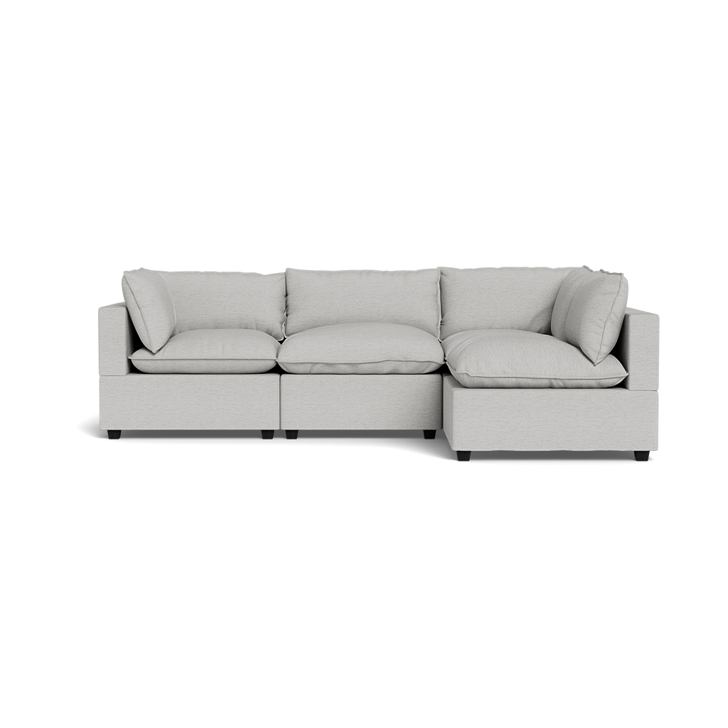 The Kova Pillow Cushion L-Shape is a modern light gray sectional sofa featuring three seat cushions and matching back and side pillows, set against a plain black background.