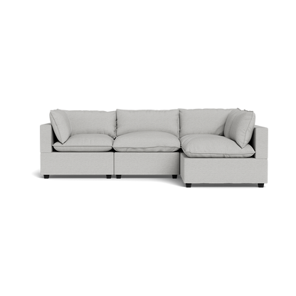 The Kova Pillow Cushion L-Shape is a modern light gray sectional sofa featuring three seat cushions and matching back and side pillows, set against a plain black background.