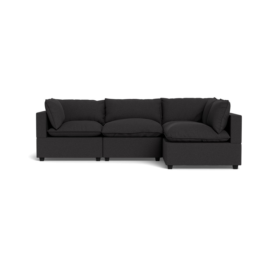 The Kova Pillow Cushion L-Shape is a modern dark grey sectional sofa with three seat, three back, and two armrest cushions, shown against a plain black background.