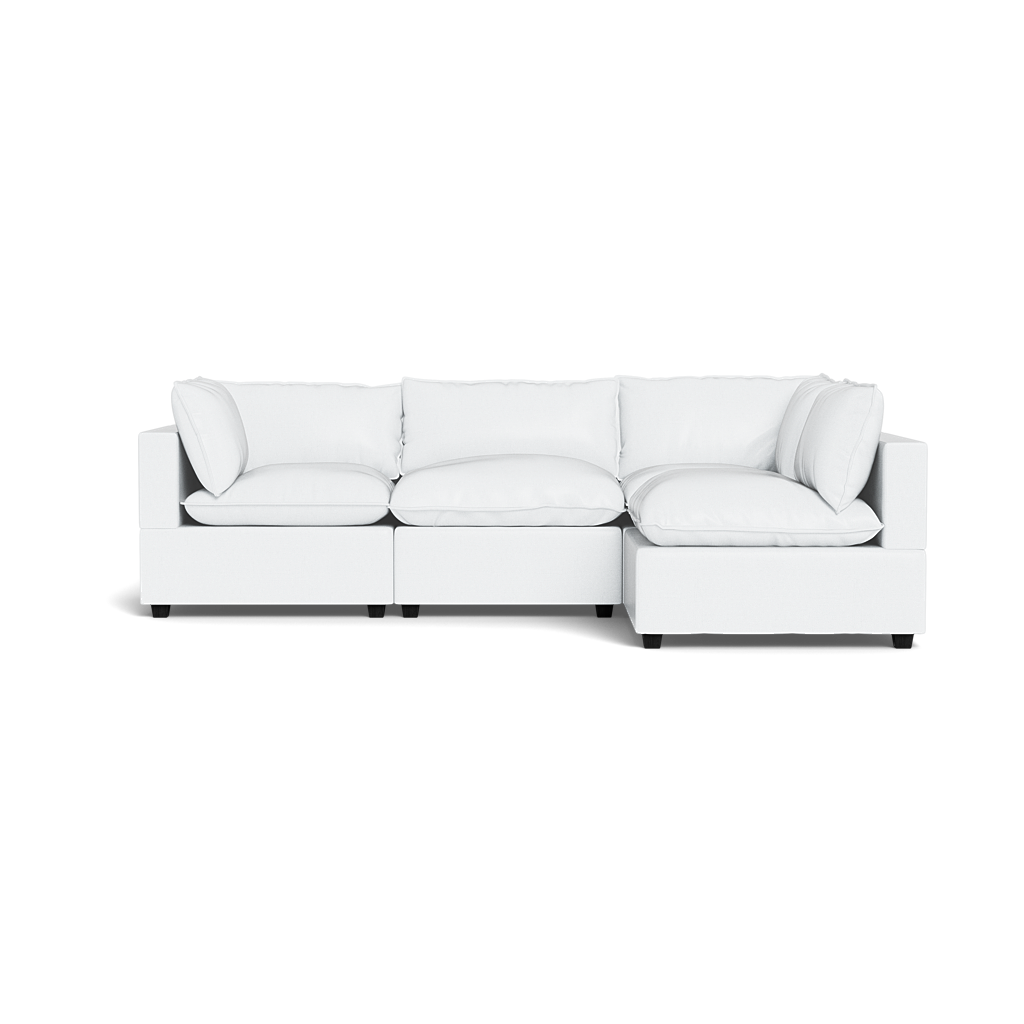 The Kova Pillow Cushion L-Shape is a modern white sectional sofa with three seat cushions and multiple matching back and side pillows, displayed against a plain black background.