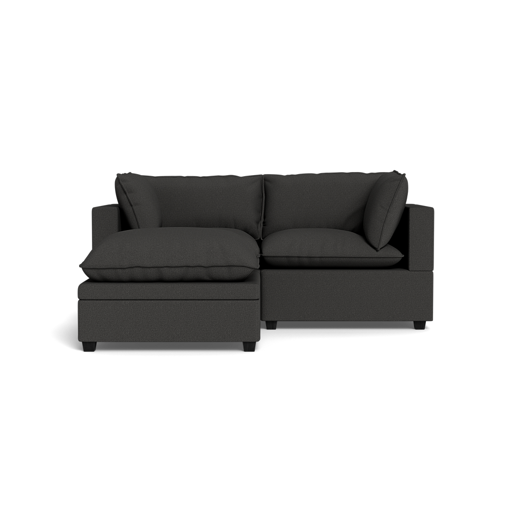 The Kova Pillow Cushion Sofa 86" with Ottoman features large cushions and a left-side chaise lounge, set against a solid black background.