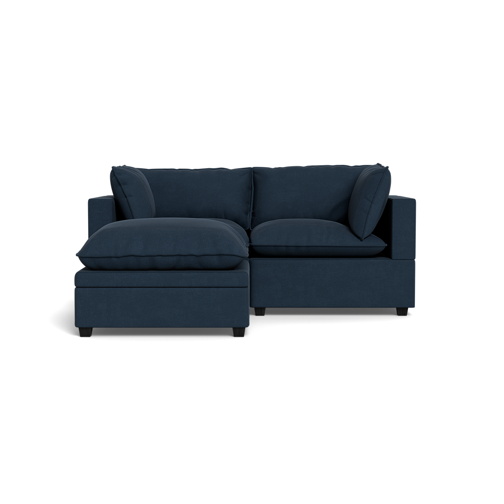 The Kova Pillow Cushion Sofa 86" + Ottoman is a modern dark blue sectional with plush cushions and a left-side chaise, set against a black background.