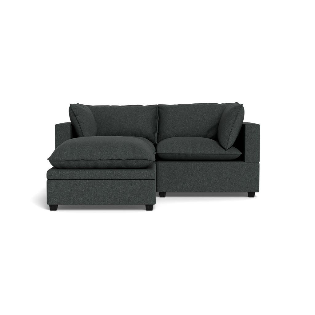 The Kova Pillow Cushion Sofa 86" + Ottoman is a modern dark gray sectional with thick cushions and a left-side chaise, shown on a black background.