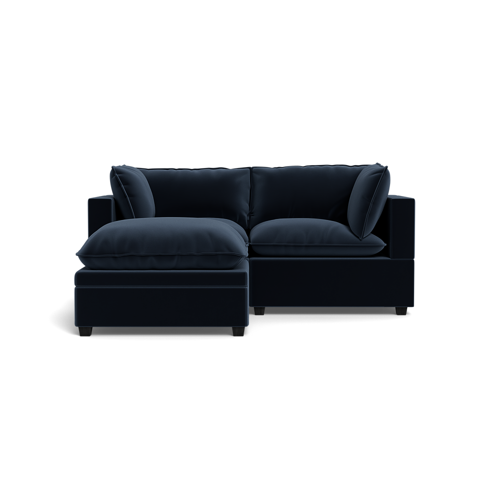 The Kova Pillow Cushion Sofa 86" + Ottoman features plush dark blue cushions and a left-facing chaise lounge, shown from the front against a black background.