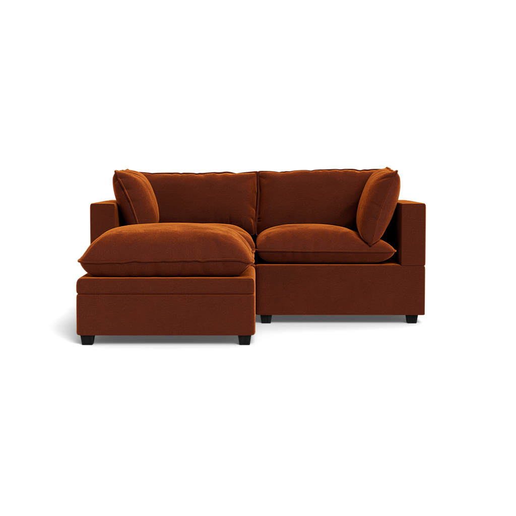 The Kova Pillow Cushion Sofa 86" with Ottoman features plush cushions and pillows in a modern rust color, showcased against a plain black background.