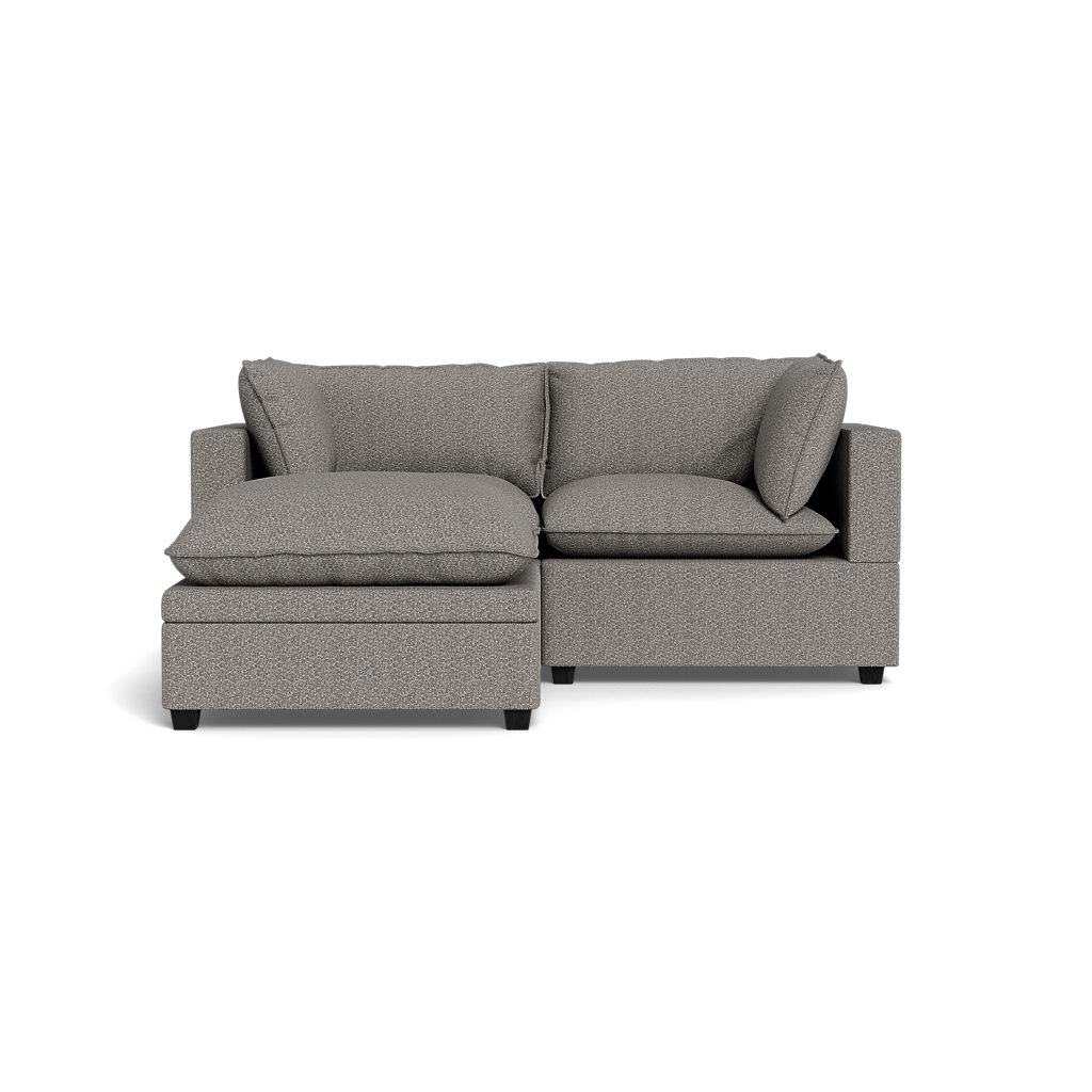 The Kova Pillow Cushion Sofa 86" with ottoman features a modern gray design, left chaise lounge, plush seat and back cushions, and two side pillows, shown against a black background.