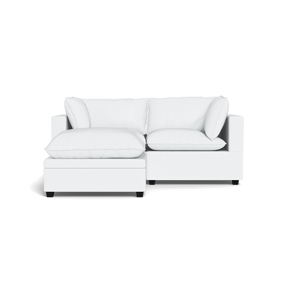 The Kova Pillow Cushion Sofa 86" + Ottoman in modern white, featuring plush cushions and pillows, is shown from the front against a black background.