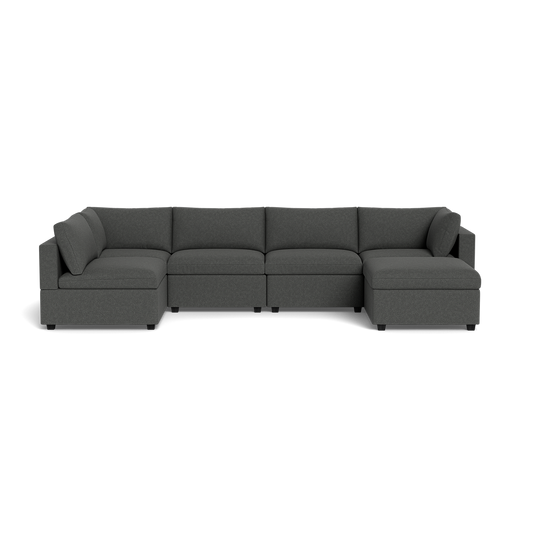 The Kova Box Cushion U-Shape is a modern, dark gray fabric sectional with five seats, featuring a right-side chaise and a left corner section, displayed against a plain black background.