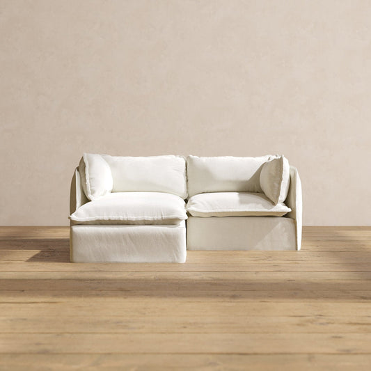A minimalist room showcasing a white Modular Performance 2-Seater Sectional with sleek lines and plush cushions. The sectional is set on a wooden floor against a beige wall, contributing to the simple and elegant aesthetic.