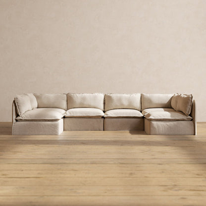 The Modular Performance 6-Seater Open-Ends U-Sectional in Plush Weave Ash features thick cushions and is set against a plain, light-colored wall. The room has light wood plank flooring that enhances the warm and minimalistic ambiance.