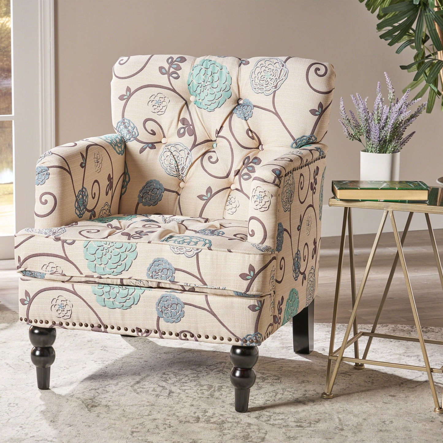 The Vitality Club Chair, featuring beige upholstery with blue and gray floral patterns, sits on a light rug beside a modern table topped with lavender. Sunlight streams in from a window, highlighting a green plant in the background.