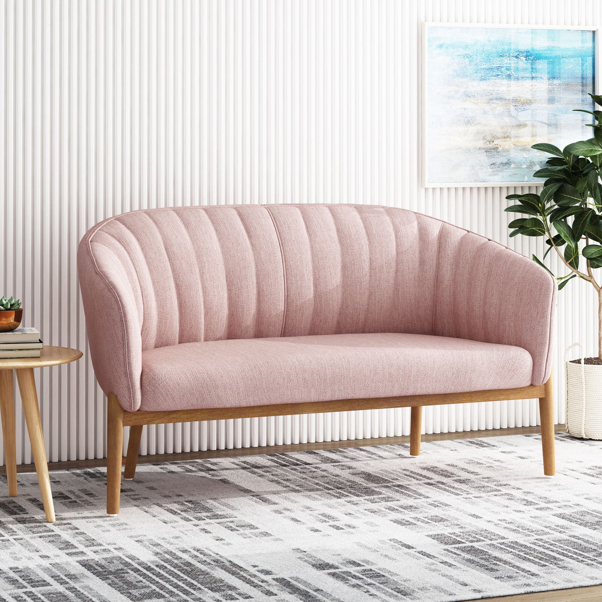 A Mid Century Modern Loveseat With Channel Stitched Backrest and wooden frame sits on a patterned rug. To the left is a round wooden side table; to the right, a green potted plant. Above, abstract art hangs on a white textured wall.