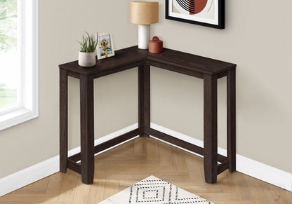 The Corner Accent Console Table For Entryway, Unique Design Contemporary & Modern, is a dark wood L-shaped table set against a beige wall by a window, topped with a lamp, plant, framed photo, and small decorative piece.
