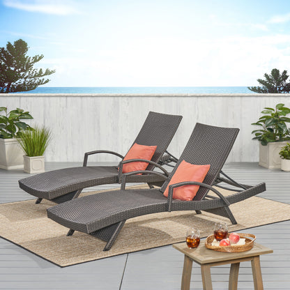 Two Salem Contemporary Wicker Chaise Lounges with arms and coral cushions sit on a patio rug by the ocean, accented with a small table holding drinks and fruit, surrounded by potted plants and white fencing. The lounges are weather resistant.