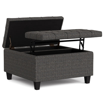 The Harrison Upholstered Coffee Table Storage Ottoman features a square shape, dark gray fabric, tufted top, hinged lid for storage access, and short black legs.
