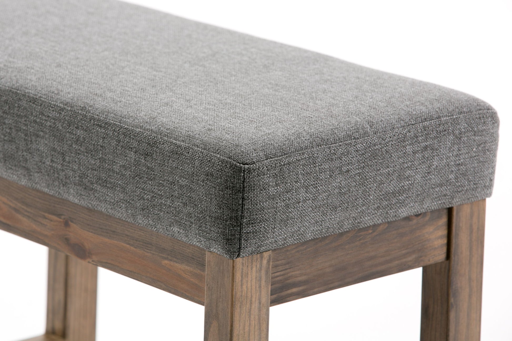 Close-up of the Milltown Upholstered Ottoman Bench, featuring a grey cushion and wooden legs, set against a plain white background.