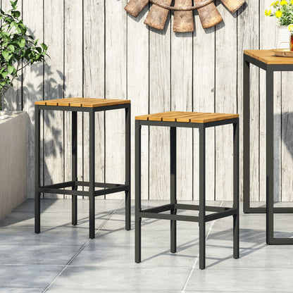 A set of two Outdoor Bar Stools with slat design and metal frames sits on a tiled patio by a rustic wooden fence, near a table and green plants, with part of a decorative wall piece above.