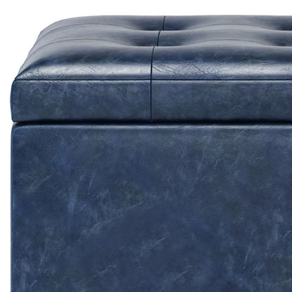 Close-up of the Cosmopolitan Upholstered Storage Ottoman in dark blue leather, featuring deep square tufting on the cushion, smooth sides with subtle marbling, visible stitching, and a textured surface.
