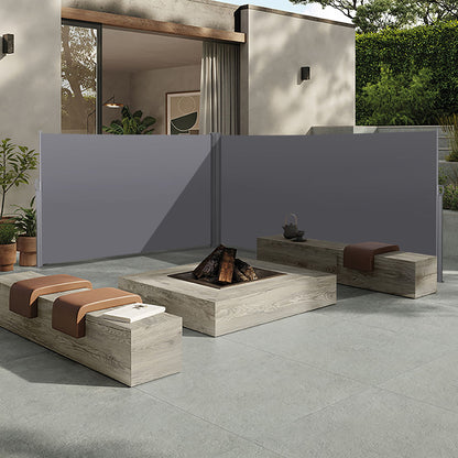Modern patio with two wooden benches, a square fire pit, potted plants, and a gray Retractable Side Awning (Waterproof & UV-Resistant Privacy Screen Divider Roll Up Balcony); house and greenery in the background.