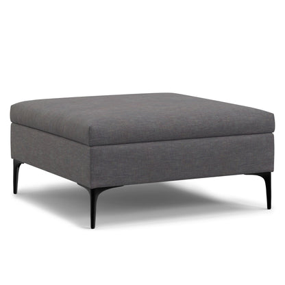 The Rebecca is a modern square storage ottoman coffee table with dark gray fabric upholstery, black metal legs, and a lift-up lid, shown against a white background.