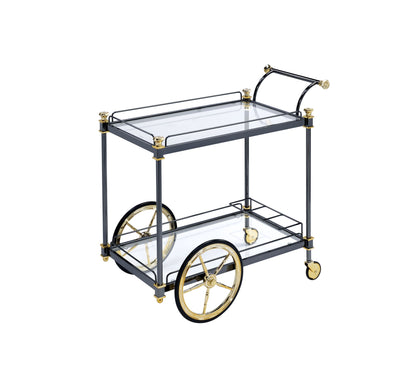 The Cyrus Clear Glass Serving Cart in Black/Gold features two glass shelves, two large decorative wheels, and a curved handle, all set against a white background.