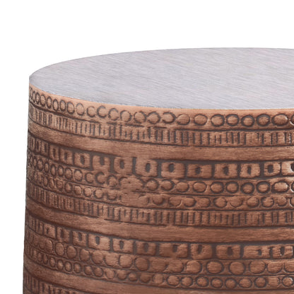 A close-up of the Johnsen Handcrafted Large Metal Accent Table shows its cylindrical shape, etched horizontal bands with circular and rectangular patterns, and a brushed copper-like finish.