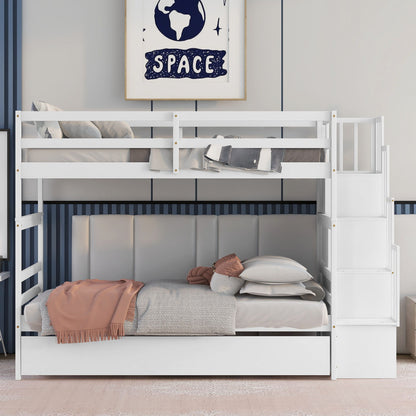 A white Twin Over Twin Bunk Bed with Trundle and Stairway Storage is neatly made with pillows and a peach blanket. The lower bunk features a padded gray headboard, and space-themed art hangs above on the wall.