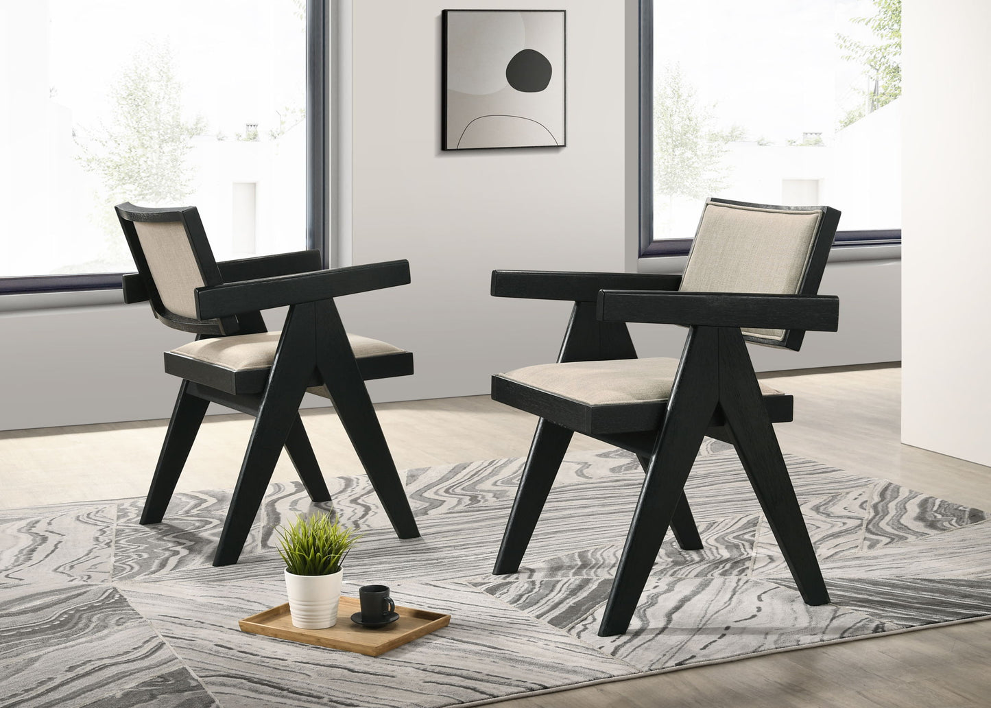 The Jasper 3 Piece Arm Chairs and Console Table (Ebony Black) set features modern angular chairs on a patterned rug in a bright, minimalist room with large windows, abstract wall art, and a tray with plant and cup.