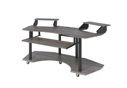 The Eleazar Music Recording Studio Desk features a modern gray wood design with two raised monitor shelves, a pull-out keyboard tray, a curved lower shelf, black metal legs, and four caster wheels for mobility.