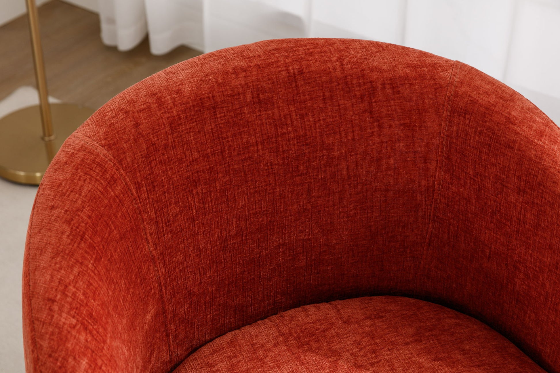 A close-up of the Chenille Fabric Swivel Accent Armchair Barrel Chair with a powder-coated metal ring, upholstered in textured red fabric, alongside a gold floor lamp and white curtains in the background.