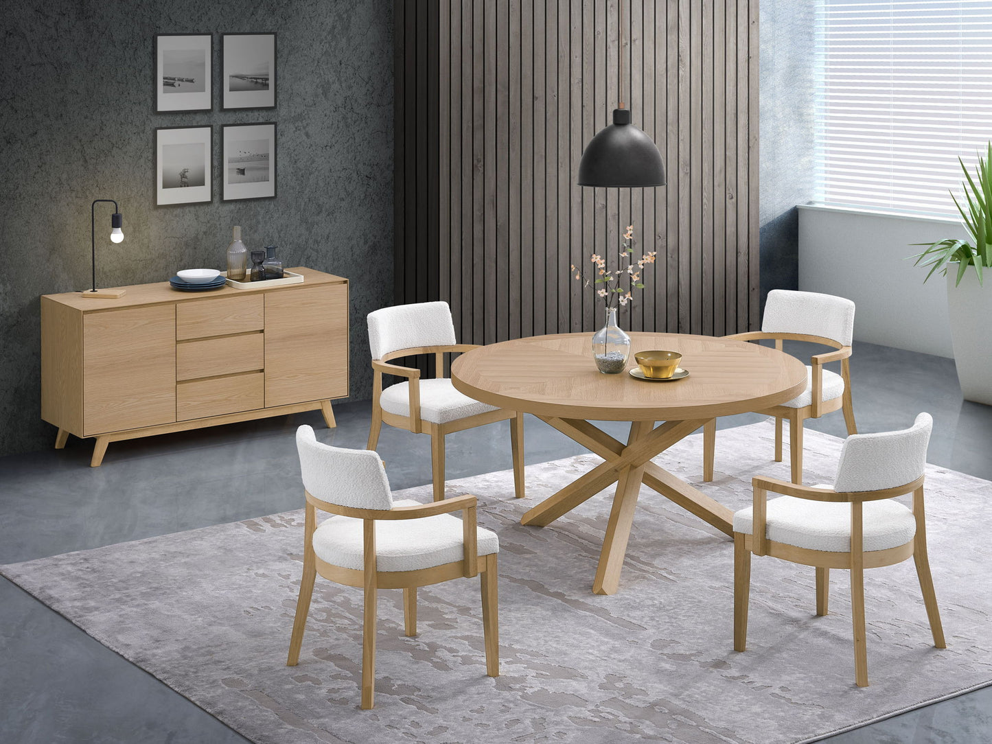 A modern dining room featuring a round wooden table, four white cushioned chairs, the Kasem - Server - Oak sideboard, framed wall art, a black hanging lamp, a rug, and a large window with blinds and a potted plant.