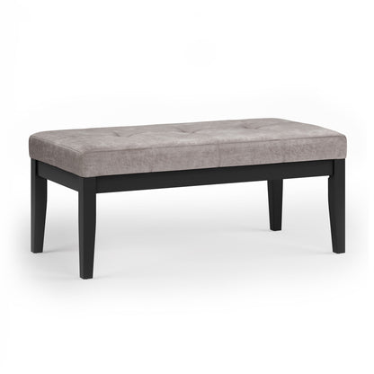 The Lacey Upholstered Tufted Ottoman Bench features a light gray cushioned, tufted seat and four black wooden legs, displayed on a white background.