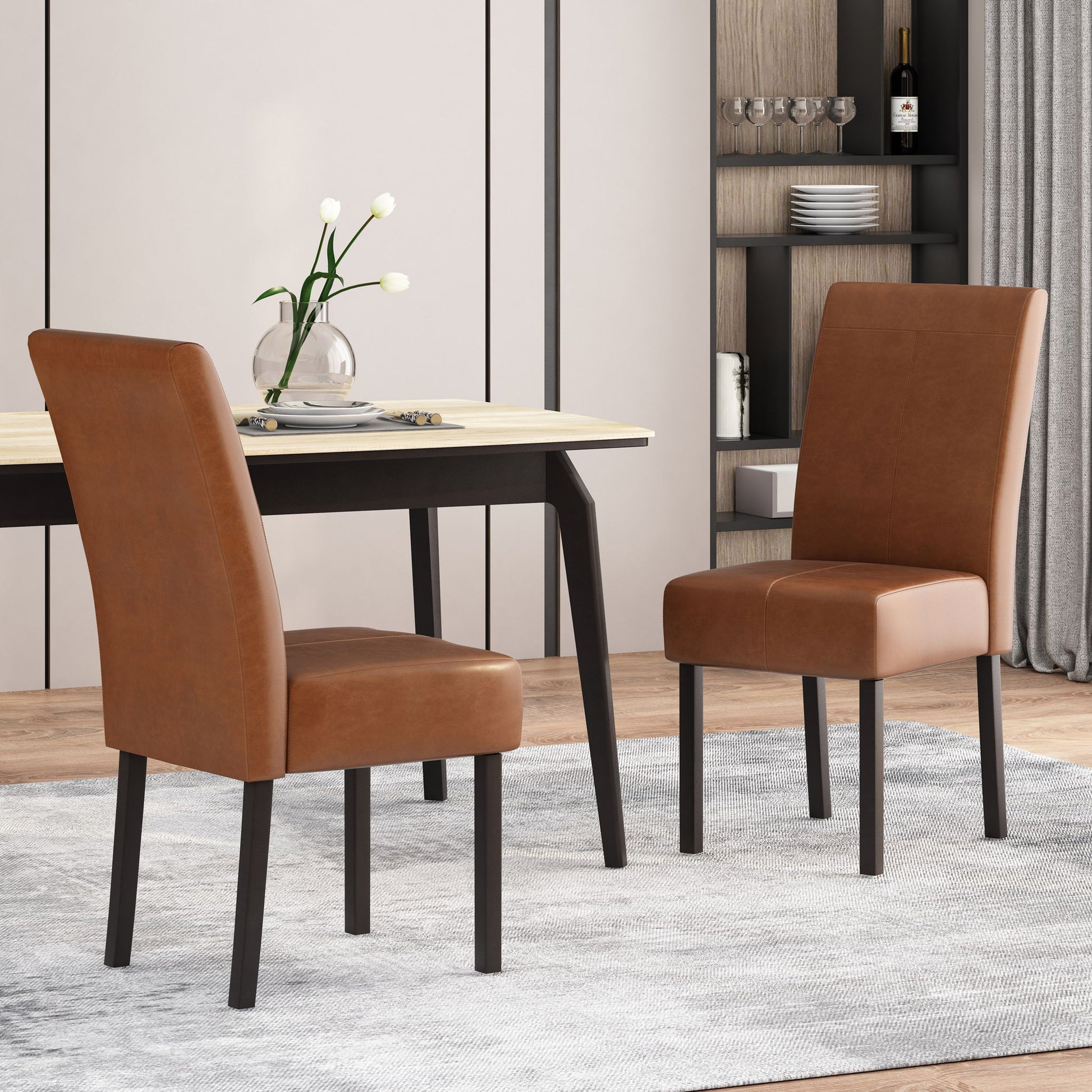 Two Pertica Dining Upholstered Armless Chairs in brown leather with dark wooden legs are set around a light wood dining table in a modern dining room, featuring a light rug, neutral walls, shelves with dishes, and a vase of white flowers.