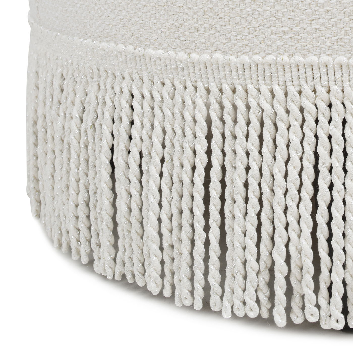 Close-up of white, twisted fringe trim hanging from the edge of the Yolanda - Round Upholstered Accent Ottoman's textured fabric surface.