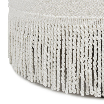 Close-up of white, twisted fringe trim hanging from the edge of the Yolanda - Round Upholstered Accent Ottoman's textured fabric surface.