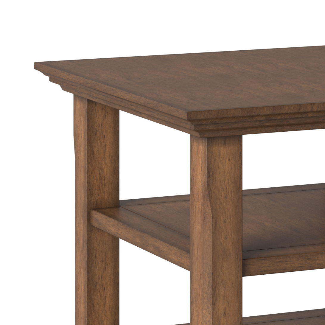 Close-up of the Acadian - Transitional End Table, showcasing its rectangular top, two lower shelves, natural brown finish, and sturdy legs. The table is set against a plain white background.