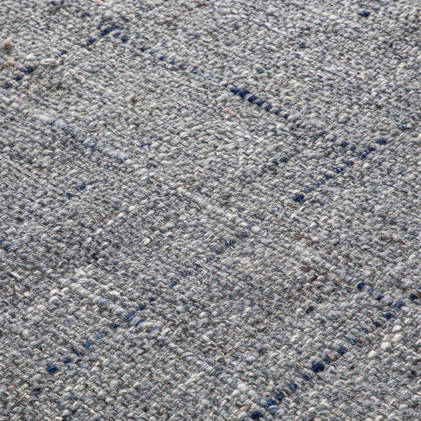 Close-up of the Tenney Handcrafted Area Rug, showcasing its textured woven fabric in gray and blue hues with a subtle grid pattern formed by intersecting raised lines.